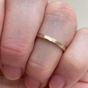 May include: A thin gold band ring with a hammered texture. The ring is worn on a finger.