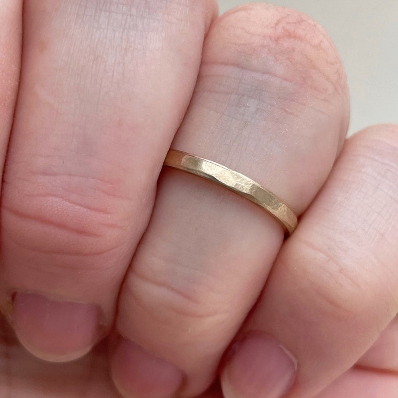 May include: A thin gold band ring with a hammered texture. The ring is worn on a finger.
