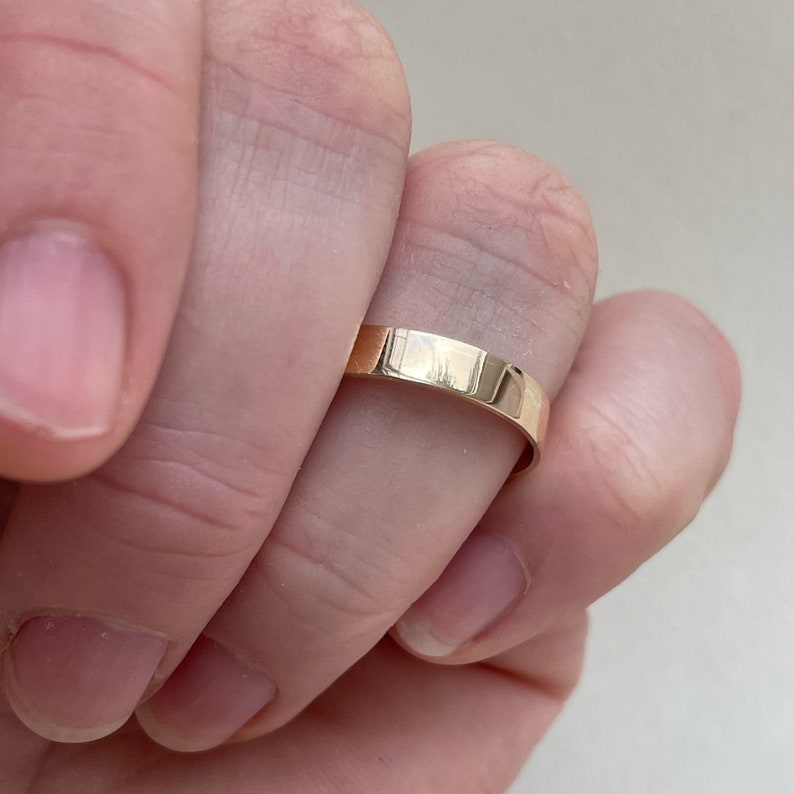 May include: A simple gold band ring worn on a finger.