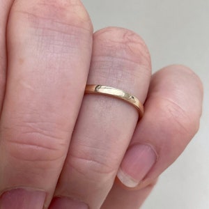 May include: A simple gold band ring worn on a finger.