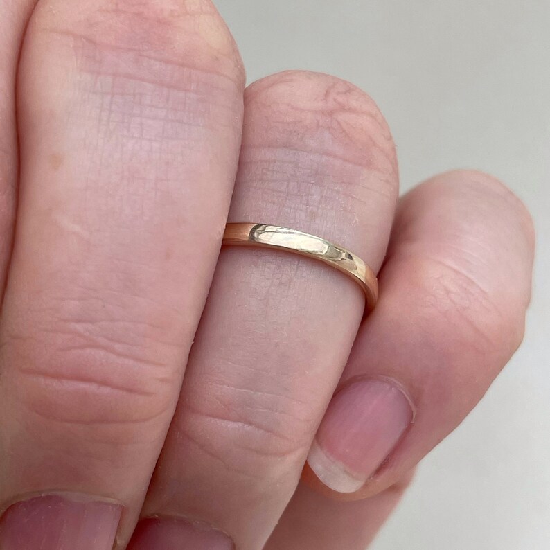 May include: A simple gold band ring worn on a finger.