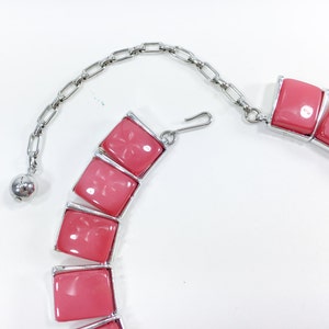May include: A pink statement necklace with a silver chain and a clasp. The necklace features large, square-shaped pink stones.