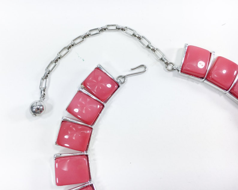 May include: A pink statement necklace with a silver chain and a clasp. The necklace features large, square-shaped pink stones.
