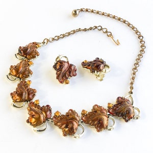 May include: A gold necklace with a brown and gold leaf design and matching earrings. The necklace has a chain with a clasp and the leaves are detailed with small rhinestones.