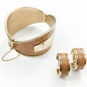 May include: A gold-toned bangle bracelet and matching earrings with a wood-grain design. The bracelet has a hinged clasp and a small chain attached. The earrings are hoop style.