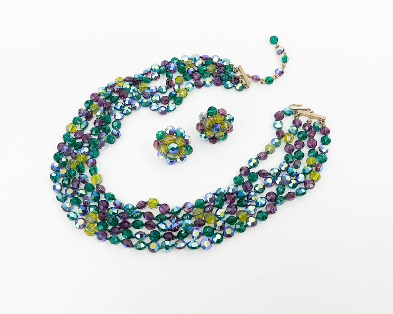 May include: A multi-strand necklace and matching earrings made of iridescent green, purple, and yellow glass beads. The necklace is layered and the earrings are cluster style.