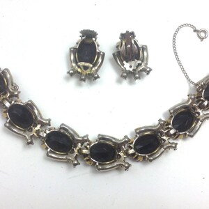 May include: A silver bracelet with a chain closure and black oval-shaped stones. Matching clip-on earrings with black oval-shaped stones.