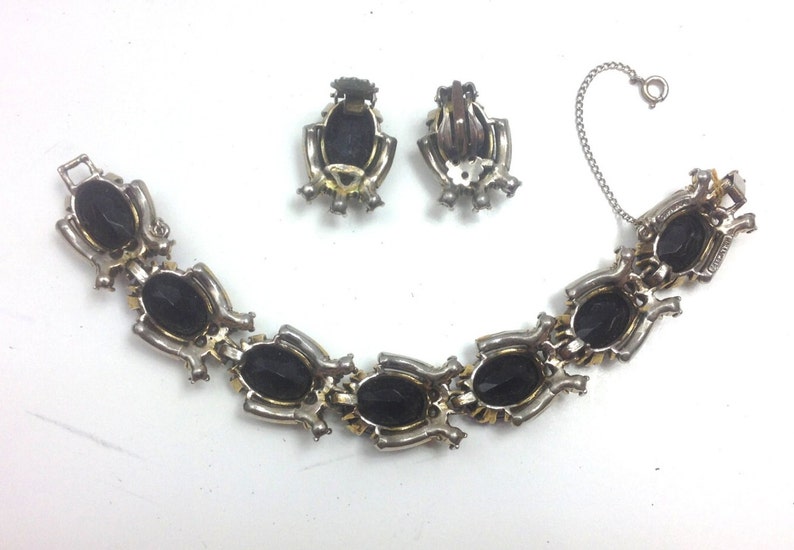 May include: A silver bracelet with a chain closure and black oval-shaped stones. Matching clip-on earrings with black oval-shaped stones.