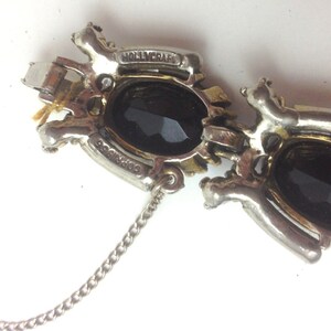 May include: A silver and gold tone bracelet with two large black oval stones. The bracelet has a chain extender and is marked "HOLLYCRAFT".