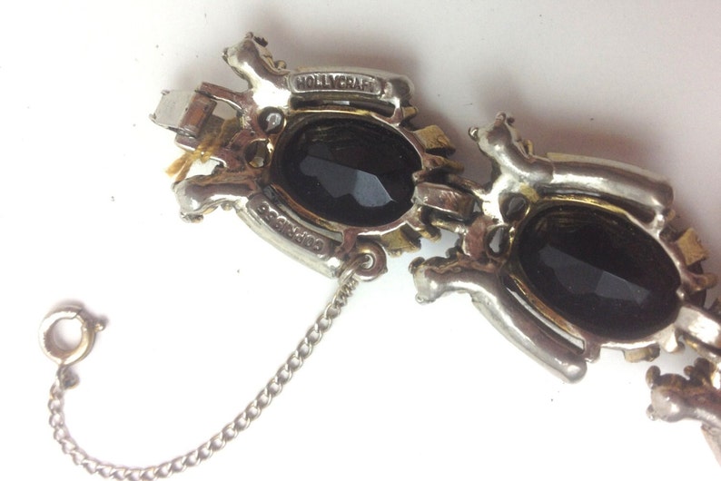 May include: A silver and gold tone bracelet with two large black oval stones. The bracelet has a chain extender and is marked "HOLLYCRAFT".