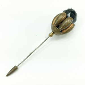 May include: A gold-toned metal pin with a black faceted glass bead at the top. The pin has a long, thin stem and a pointed end.