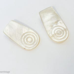 May include: Two white, oval-shaped, decorative buttons with a concentric circle design.