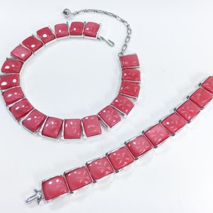 May include: A pink and silver necklace and bracelet set. The necklace and bracelet are made of square-shaped pink stones with a floral design.