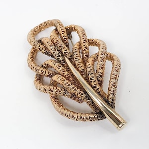 May include: A gold-toned brooch in the shape of a stylized leaf, made of interwoven wire.