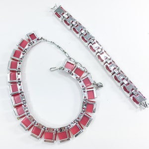 May include: A pink and silver necklace and bracelet set. The necklace and bracelet are made of linked metal squares with pink stones in the center of each square.