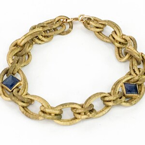 May include: A gold chain bracelet with two blue square-shaped gemstones. The chain is made of woven metal links.