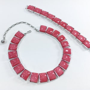 May include: A pink and silver necklace and bracelet set with large, square-shaped stones. The necklace has a chain closure and the bracelet has a clasp closure.