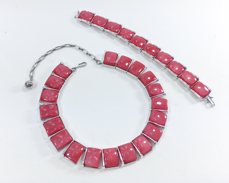 May include: A pink and silver necklace and bracelet set with large, square-shaped stones. The necklace has a chain closure and the bracelet has a clasp closure.