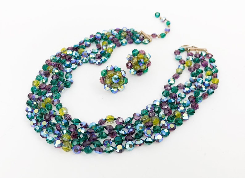 May include: A multi-strand necklace and matching earrings made of iridescent green, blue, and purple glass beads. The necklace is made of five strands of beads and the earrings are made of clusters of beads.