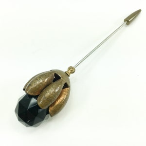May include: A vintage black glass and brass hat pin with a pointed metal tip. The pin features a faceted black glass ball topped with a brass flower design.