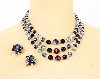 May include: A three-strand necklace and matching earrings made of clear, black, red and blue crystal beads.
