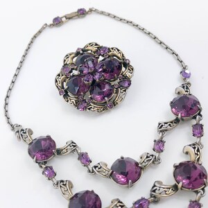 May include: A silver and gold necklace with a large purple rhinestone flower pendant and smaller purple rhinestones throughout the chain.