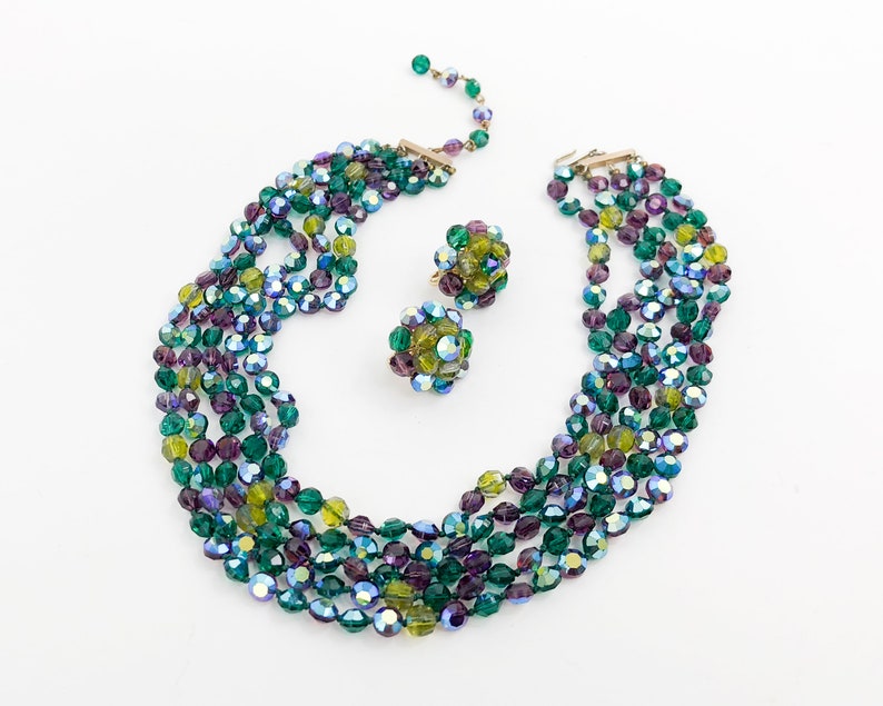 May include: A multi-strand necklace and earrings set made of green, purple, and blue iridescent glass beads. The necklace is made of five strands of beads and the earrings are made of a cluster of beads.