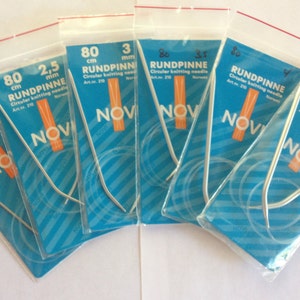 May include: Five packages of circular knitting needles in various sizes, labeled "RUNDPINNE" with the size and length in millimeters and centimeters. The needles are silver and packaged in clear plastic bags with blue and orange labels.
