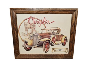 May include: A framed print of a vintage Chrysler Model 70 Roadster, a yellow and brown car with a tan convertible top, set against a background of the Arc de Triomphe in Paris. The print is titled "Chrysler 1930 Model 70 Roadster".