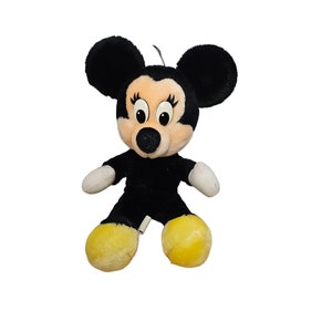 May include: A black and white plush Mickey Mouse toy with yellow shoes. The toy has a big smile and large eyes.