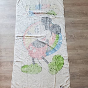 May include: A white beach towel with a colorful Mickey Mouse design. The towel features a rainbow circle around Mickey Mouse, who is wearing red shorts and green shoes. The towel has the text "Disney" printed on the bottom right corner.