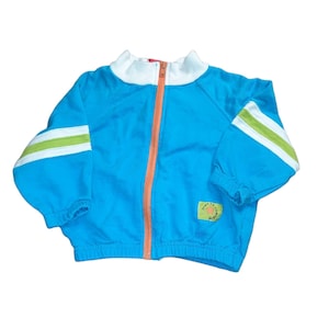 May include: A blue zippered jacket with white and green stripes on the sleeves. The jacket has a white collar and a small orange patch with the text "Don't Go To Sleep" on the front.