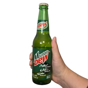 May include: A green glass Mountain Dew bottle with a silver cap. The bottle has a green and white label with the Mountain Dew logo and signatures. The bottle contains 12 fl oz (355 ml) of soda.