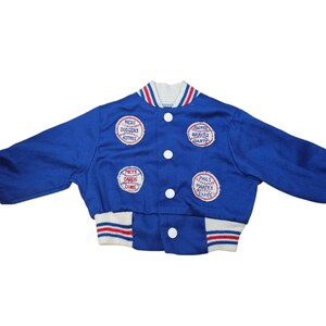 May include: A blue vintage baseball jacket with white, red, and blue striped trim. The jacket features patches with team names like Mets, Dodgers, and Braves. It has a button-up front and white buttons.