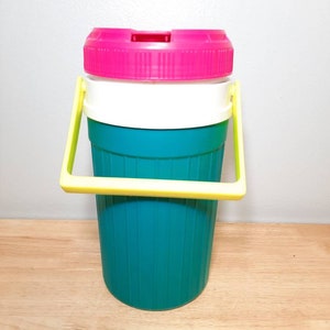 May include: A teal and white insulated beverage container with a pink lid and a yellow handle.