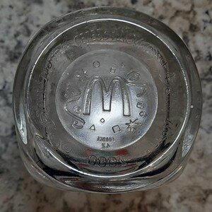 May include: The bottom of a clear glass cup with the McDonald's logo and the words "McDonald's Corporation" printed on the bottom.