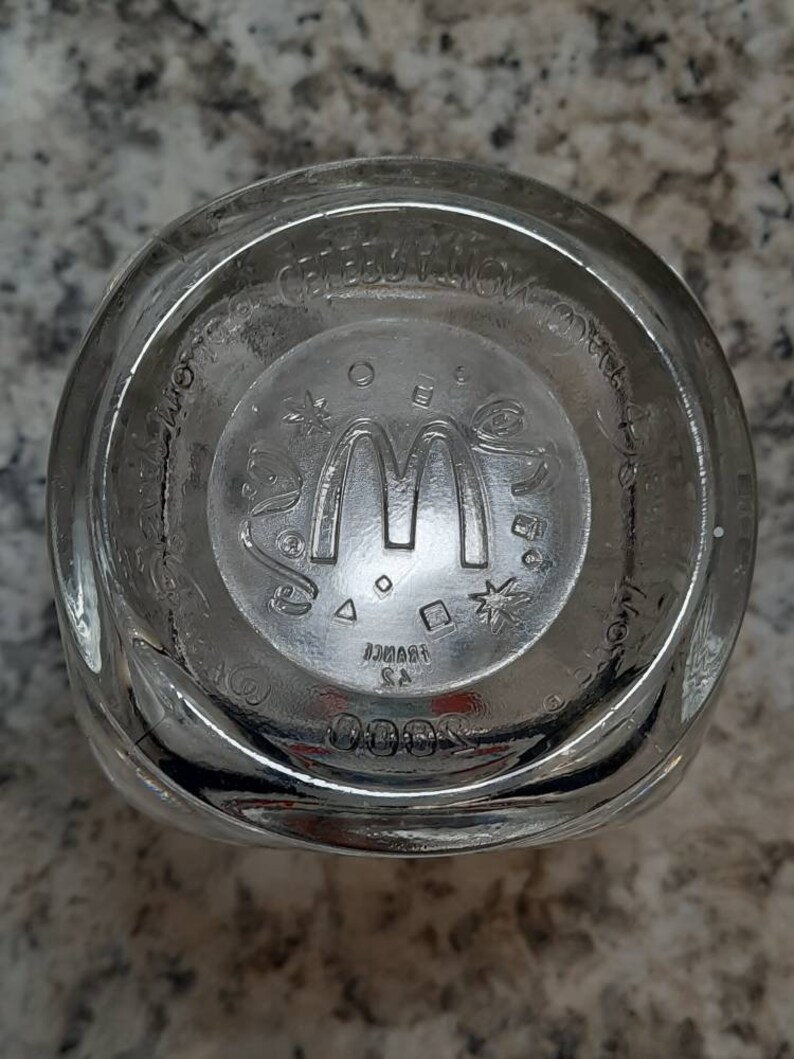 May include: The bottom of a clear glass cup with the McDonald's logo and the words "McDonald's Corporation" printed on the bottom.