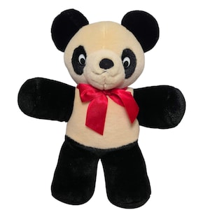 May include: A plush panda bear with a cream-colored face and body, black ears, arms, and legs. The panda has a red satin bow tied around its neck. The bear is standing upright with its arms outstretched.