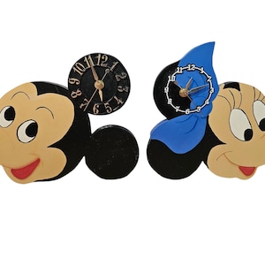 May include: Wooden Mickey and Minnie Mouse wall clocks. Mickey's clock has a black face with gold hands, while Minnie's has a blue bow and a white clock face. Both clocks are in the shape of the characters' heads.
