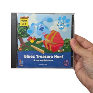 May include: A Blue's Clues Blue's Treasure Hunt A Learning Adventure Win/Mac CD-ROM in a clear plastic case. The cover features a blue dog character, a red treasure chest, a small bee, and a yellow notepad icon with the text ages 3-6.