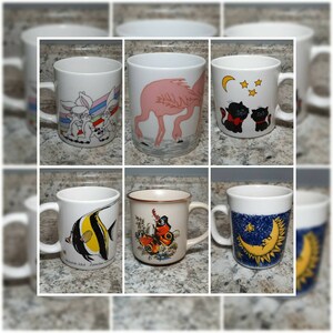 May include: Six white ceramic mugs with different colorful designs. The mugs feature a pink flamingo, two black cats, a butterfly, a fish, and a crescent moon and sun.