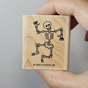 Pode incluir: Um carimbo de madeira com um desenho a tra&ccedil;o preto de um esqueleto a dan&ccedil;ar. O esqueleto tem um cr&acirc;nio redondo e est&aacute; posicionado com os bra&ccedil;os e pernas estendidos. O texto "&copy; 1999 STAMPIN' UP!" est&aacute; impresso abaixo.