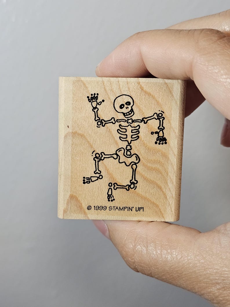 Pode incluir: Um carimbo de madeira com um desenho a tra&ccedil;o preto de um esqueleto a dan&ccedil;ar. O esqueleto tem um cr&acirc;nio redondo e est&aacute; posicionado com os bra&ccedil;os e pernas estendidos. O texto "&copy; 1999 STAMPIN' UP!" est&aacute; impresso abaixo.