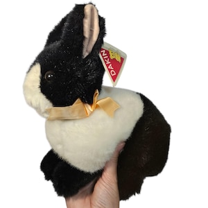 May include: A plush black and white bunny rabbit toy with a cream-colored bow. The toy has a tag that reads "DAKIN". The bunny is a stuffed animal.