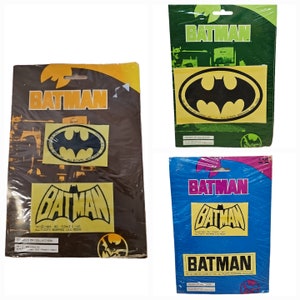 May include: Three packages of Batman iron-on patches. The packages are yellow, green, and blue with black text and images. The patches feature the Batman logo and a black bat silhouette.