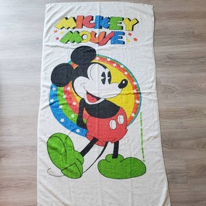 May include: White beach towel with a colorful Mickey Mouse design. The towel features Mickey Mouse walking with a red and yellow circle around him. The text "Mickey Mouse" is printed in rainbow colors at the top of the towel.