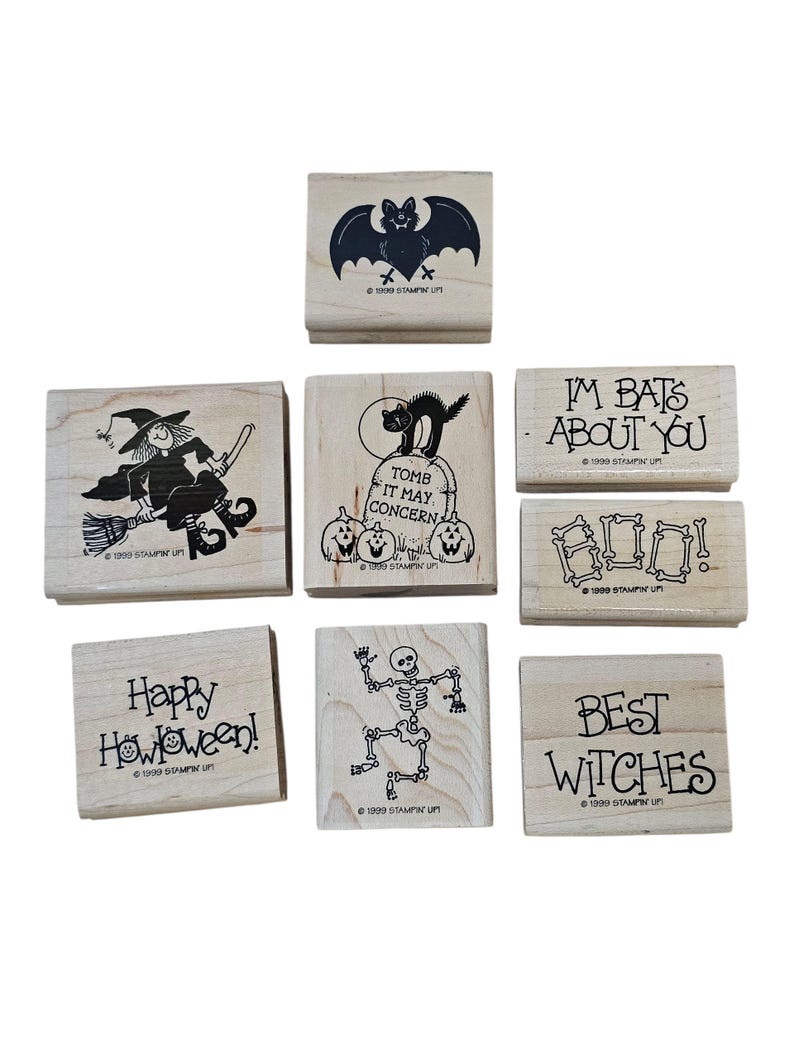 Pode incluir: Uma cole&ccedil;&atilde;o de carimbos de madeira com tema de Halloween. Os desenhos incluem um morcego, uma bruxa numa vassoura, um gato numa l&aacute;pide, um esqueleto e frases como "Happy Halloween!" e "Best Witches". Cada carimbo tem um desenho em tinta preta.