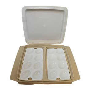 May include: A beige plastic egg holder with a white lid. The holder has two rows of six egg-shaped compartments.