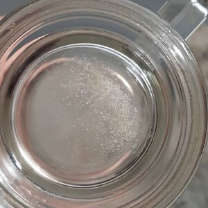 May include: Close-up of the inside of a clear glass mug with a thick rim. The bottom of the mug has a white, cloudy residue.