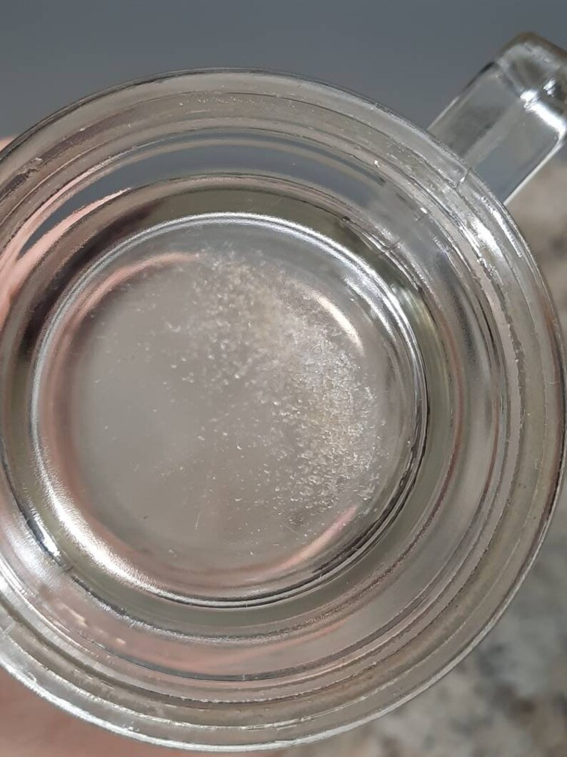May include: Close-up of the inside of a clear glass mug with a thick rim. The bottom of the mug has a white, cloudy residue.